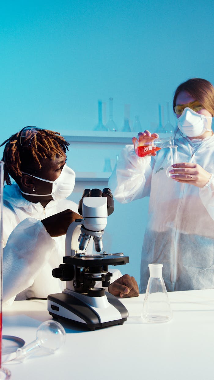 Two scientists in PPE conducting an experiment with a microscope and lab equipment.